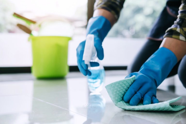 Husband housekeeping and cleaning concept, Happy young man in blue rubber gloves wiping dust using a spray and a duster while cleaning on floor at home