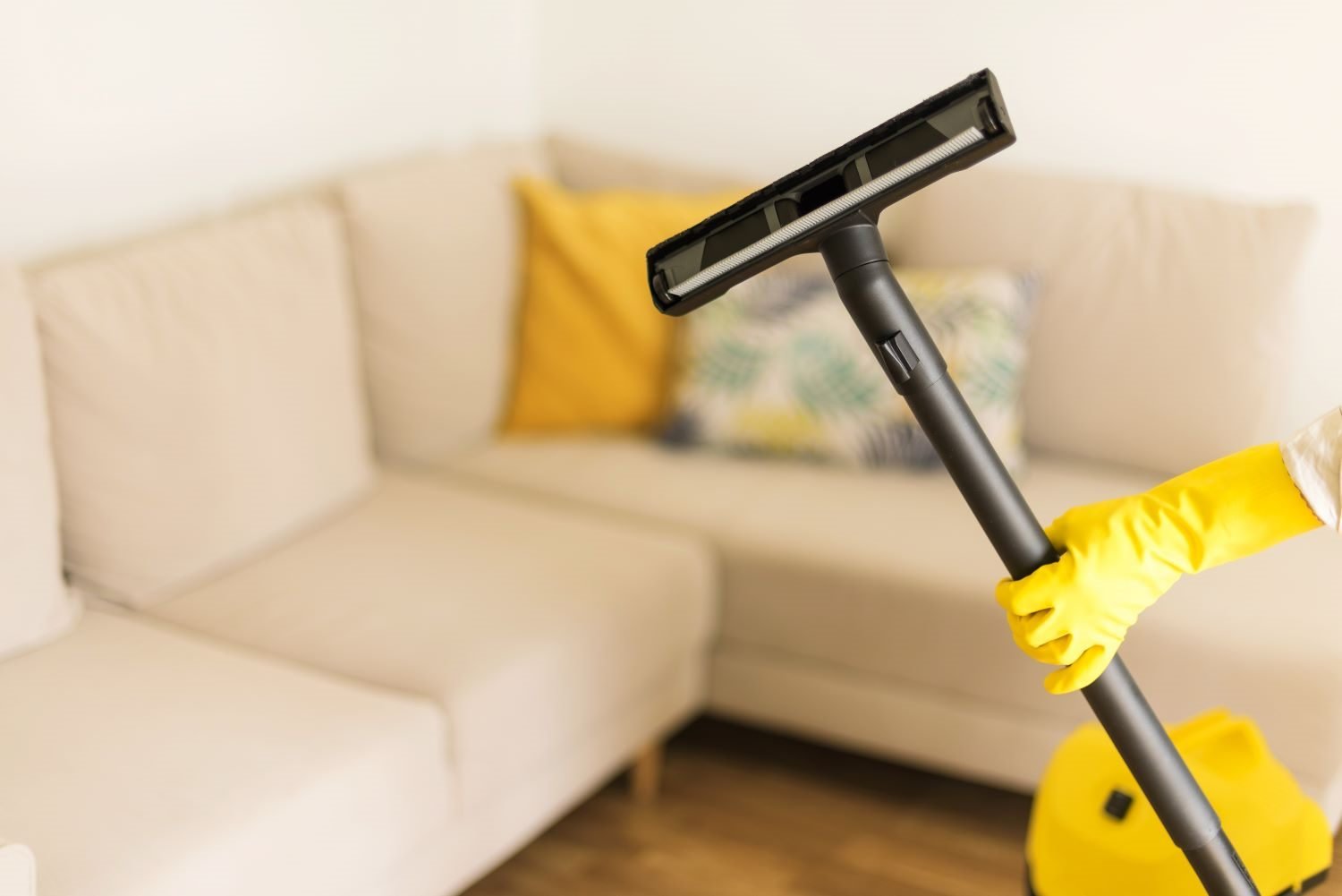 Reinigungskraft saugt ein Wohnzimmer vor der feuchten Bodenreinigung